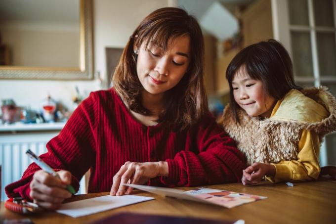 ung söt mamma skriver gratulationskort för familj med sin vackra dotter hemma