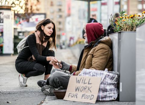 Ung kvinna som ger pengar till hemlös tiggerman som sitter i staden.