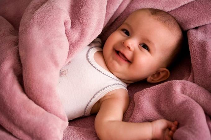 porträtt av baby i en vit tank stil skjorta leende och insvept i en mjuk rosa filt
