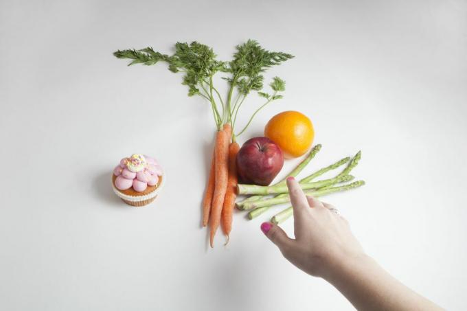 en hand sträcker sig efter ett urval av frukter och grönsaker istället för en cupcake