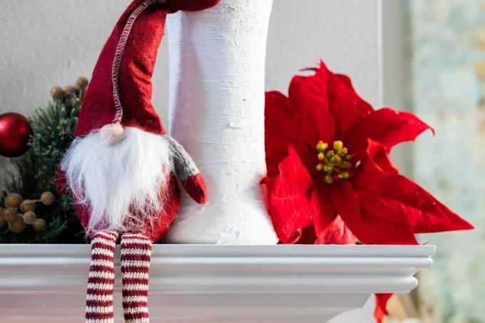 en klassisk norsk jultomtardekoration som sitter på en vit modern mantel med en vit vas med eukalyptus och en julstjärnablom