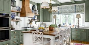 kök med lugnande grönmålade skåp, takbjälkar och inredning i kombination med vita panelväggar, tak och ö