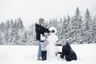 familj på tre som bygger en snögubbe i snön