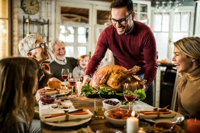 glad man serverar rostad kalkon till sin familj under Thanksgiving middag vid matbordet