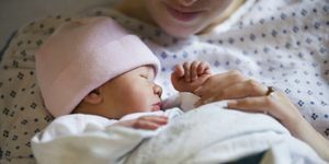 nyfödd flicka i rosa keps, insvept i en filt med mamma sett från hakan och ner i en sjukhusklänning som håller henne
