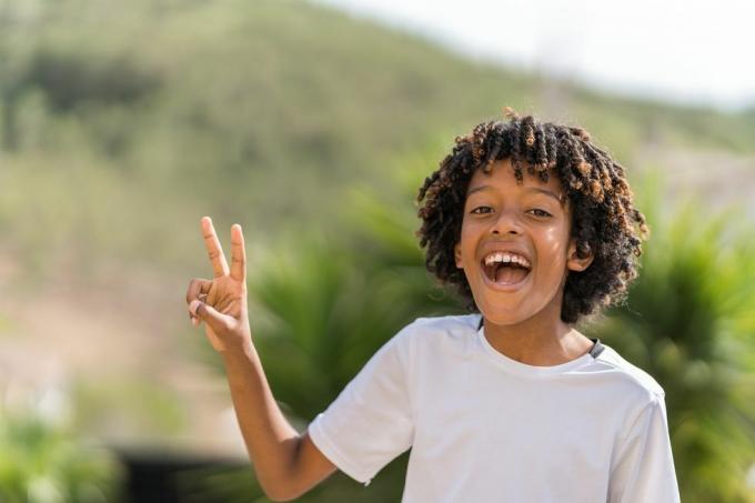 10-årig afrikansk amerikansk pojke som skrattar högt medan han gör fredstecknet