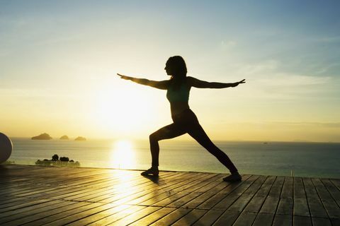 Kvinna som gör yoga vid havet vid solnedgången