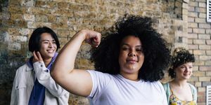 ung kvinna böjande muskler med manliga och kvinnliga vänner i bakgrunden