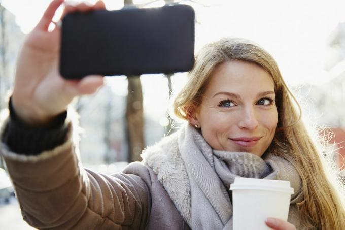 stilig kvinna som går på stadens gator på vintern och tar en selfie och håller en kaffe to go, bakgrundsbelyst