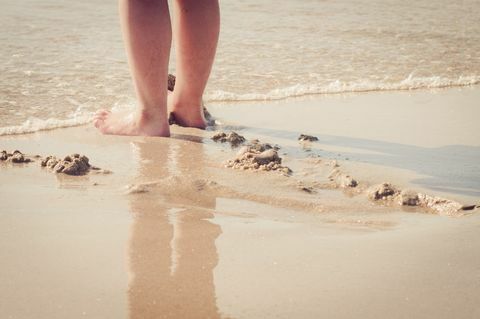 Närbild av kvinnans fötter i handen på stranden - havet som kommer in