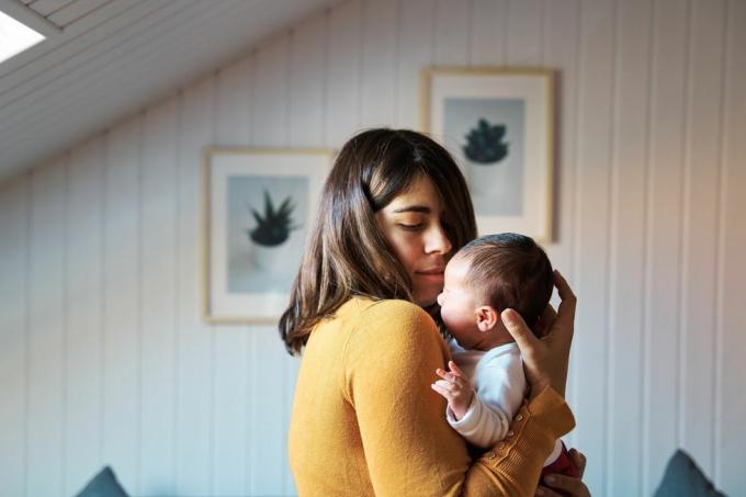 sidovy av nybliven mamma som tröstar sin nyfödda medan den gråtande bebisen vänjer sig vid ljud och ljus under sina första dagar av livet utanför livmodern