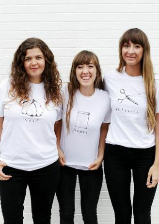tre kvinnor i vita t-skjortor, med antingen sten, papper eller sax skrivna och avbildade på skjortan