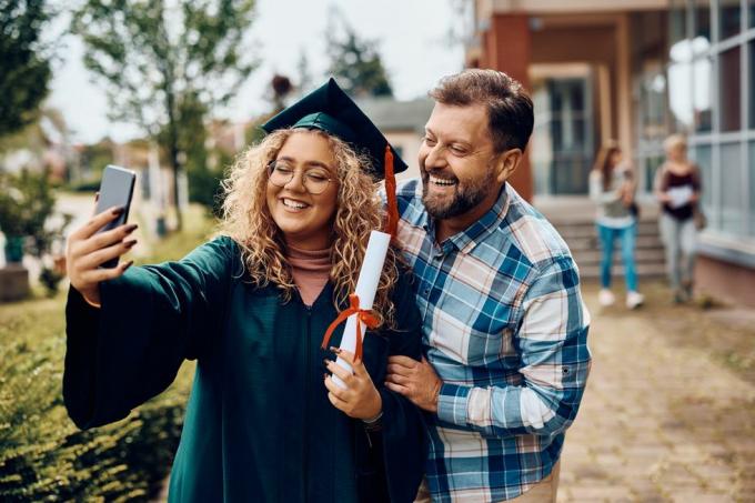 glad universitetsexamen och hennes far har roligt när hon tar selfie med smart telefon