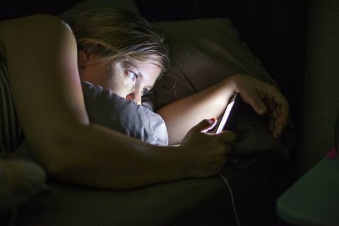 Kvinna som ser den smarta telefonen i sängen
