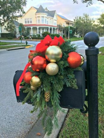 svart brevlåda och stolpe draperad med julgrönhet med guld- och röda julkulor, en kotte och en röd sammetbåge