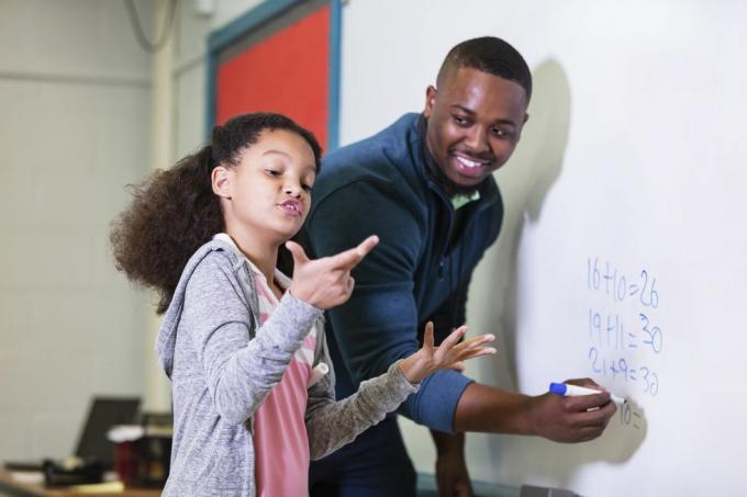 en multiracial 9-årig flicka i matematikklass, står vid whiteboarden med sin lärare, en ung afroamerikansk man i hans 20-talet läraren tittar på sin lågstadieelev och väntar medan hon försöker ta reda på svaret fokus ligger på flicka