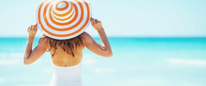 ung kvinna i hatt stående på stranden bakifrån