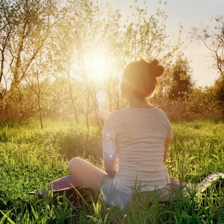 ung kvinna som sitter i yogaställning och njuter av solnedgången i naturen