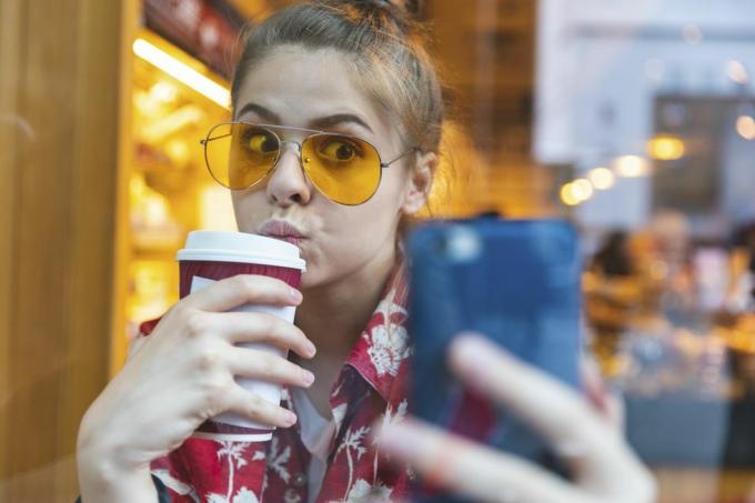 ung kvinna utanför i solglasögon som tar en selfie medan hon dricker en to go-kaffe