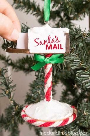prydnad som hänger på ett julgran format som en brevlåda med vit och röd randig stolpe och låda som läser jultomten är dörren till lådan öppen och en hand skjuter ett papper in i låda