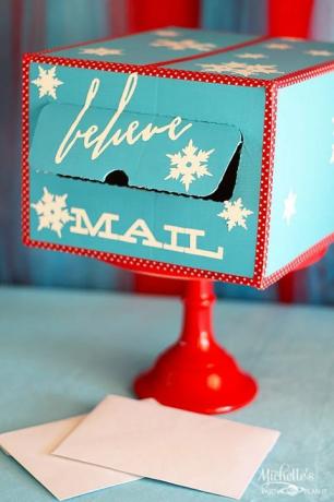 en himmelsblå fyrkantig brevlåda med "tro" och "post" skrivet i den med vita bokstäver, med vitt snöflingor och röda och vita prickiga kanter, sitter på en röd tårta med vita kuvert nedan den