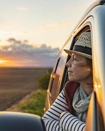 en kvinna i 40-årsåldern tar in utsikten över landskapet från sin husbil hon ser nöjd och avslappnad ut