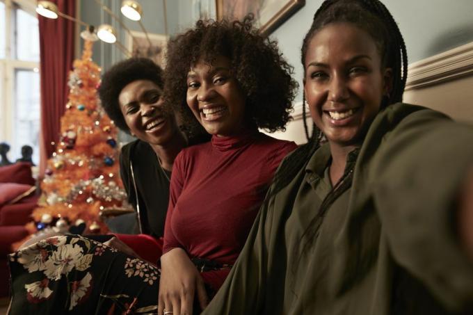 tre unga kvinnor gör selfie i soffan vid julgranen hemma
