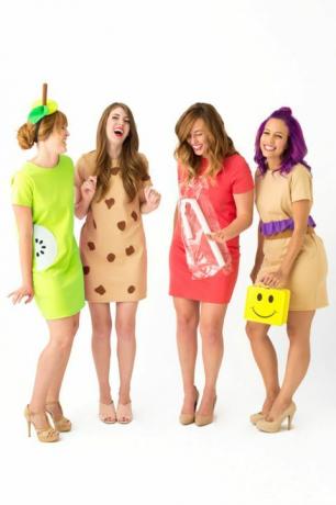 fyra skrattande kvinnor i korta klänningar klädda som "lunchdamer", en som bär en gul smiley-matlåda